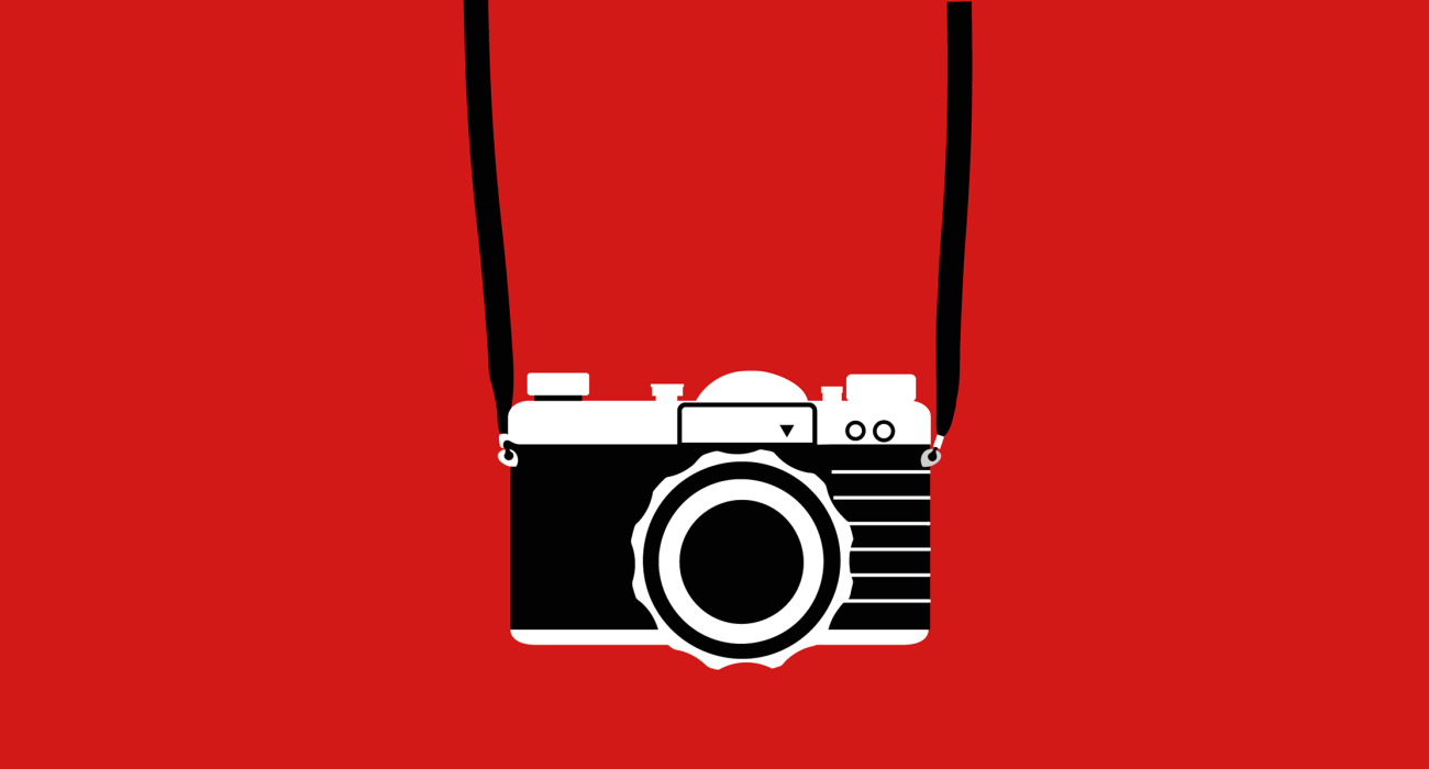 A simple line graphic of a 35mm camera hanging from a neckstrap and positioned as if it being worn by the wearer of the shirt. My god quite the optical illusion